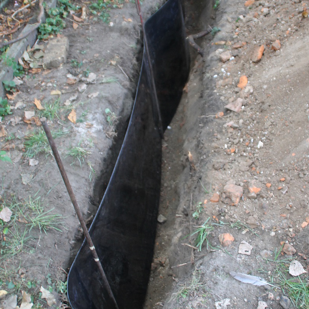 Bild von länglicher ca. 1m tiefer Grabung in einem Hinterhof, mit eingesetzter schwarzer Wurzelschutzfolie.